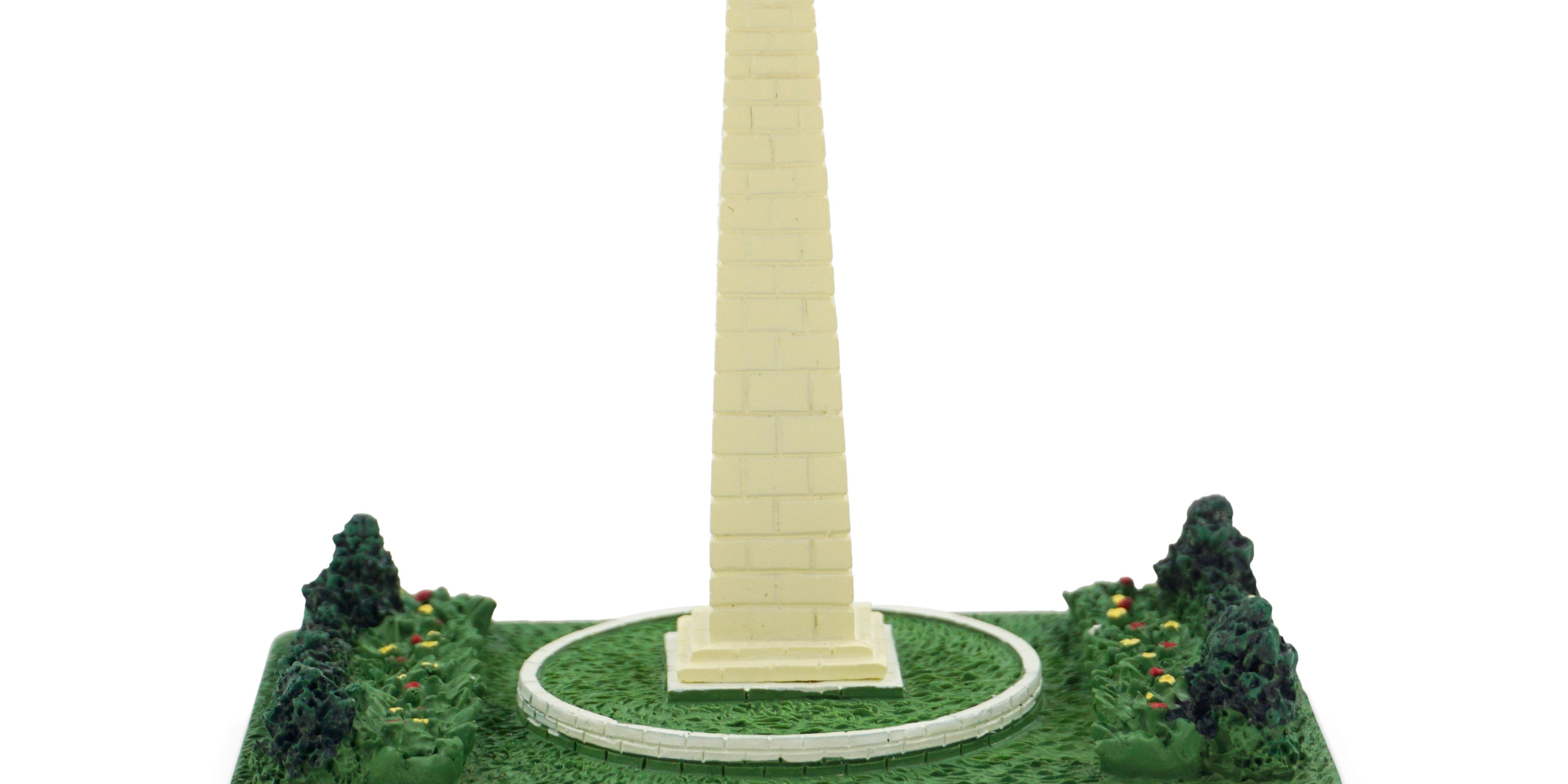 Model of the Washington Monument on a green base with trees, on a white background