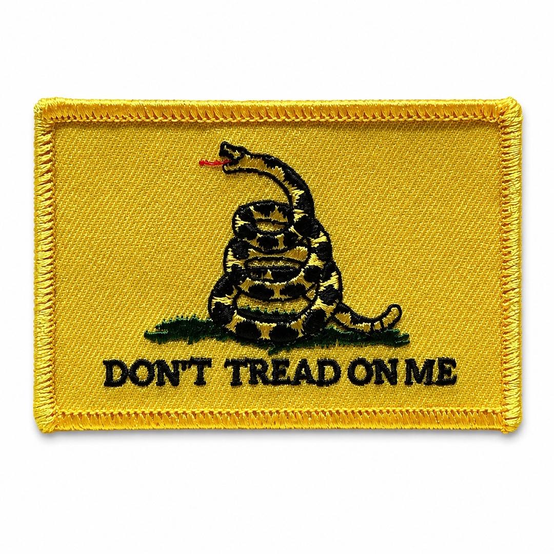 A rectangular yellow embroidered patch featuring a coiled rattlesnake with the text 'DON'T TREAD ON ME' in black, on a plain white background.
