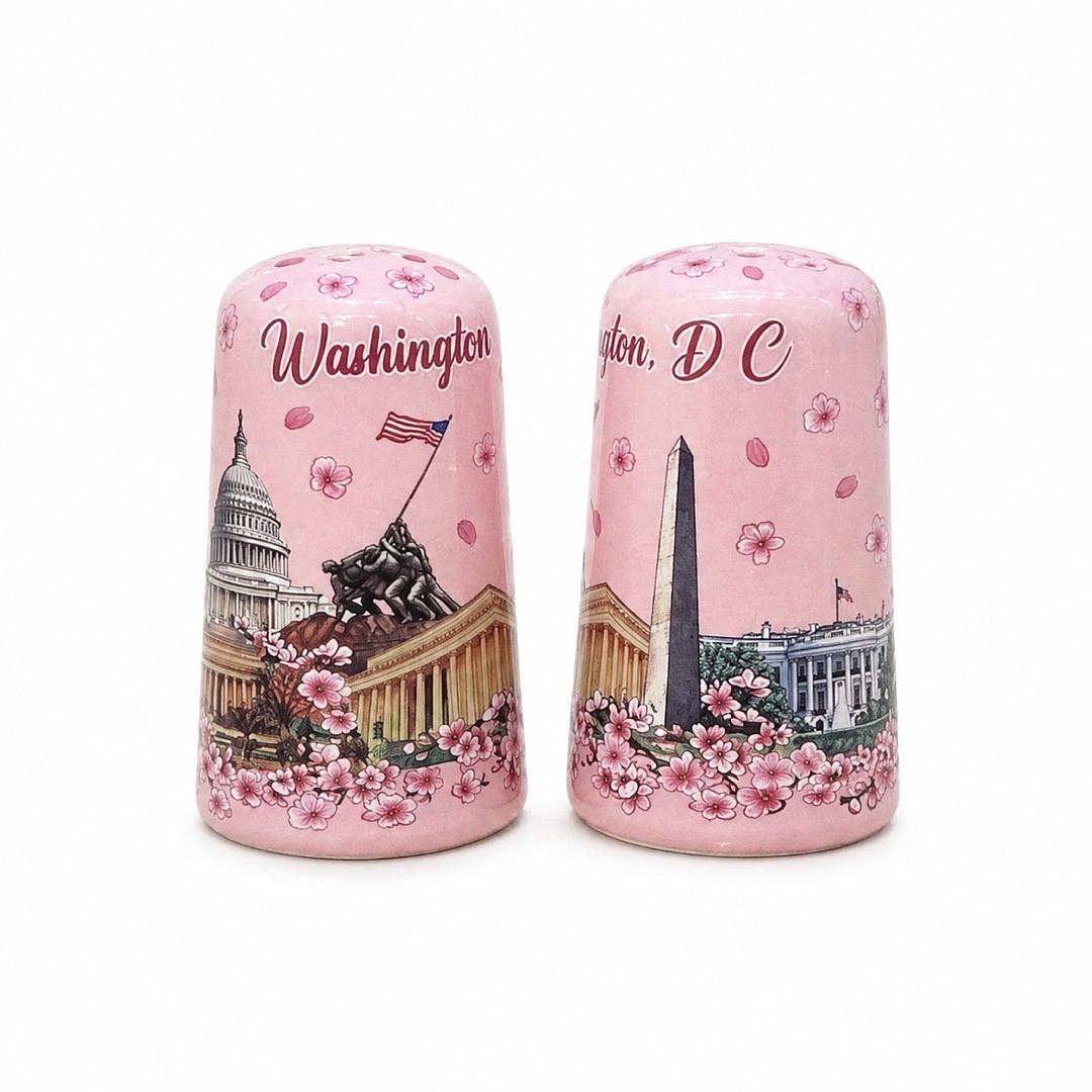 A pair of pink ceramic salt and pepper shakers decorated with cherry blossom patterns and a small architectural illustration near the base, shown on a plain white background.