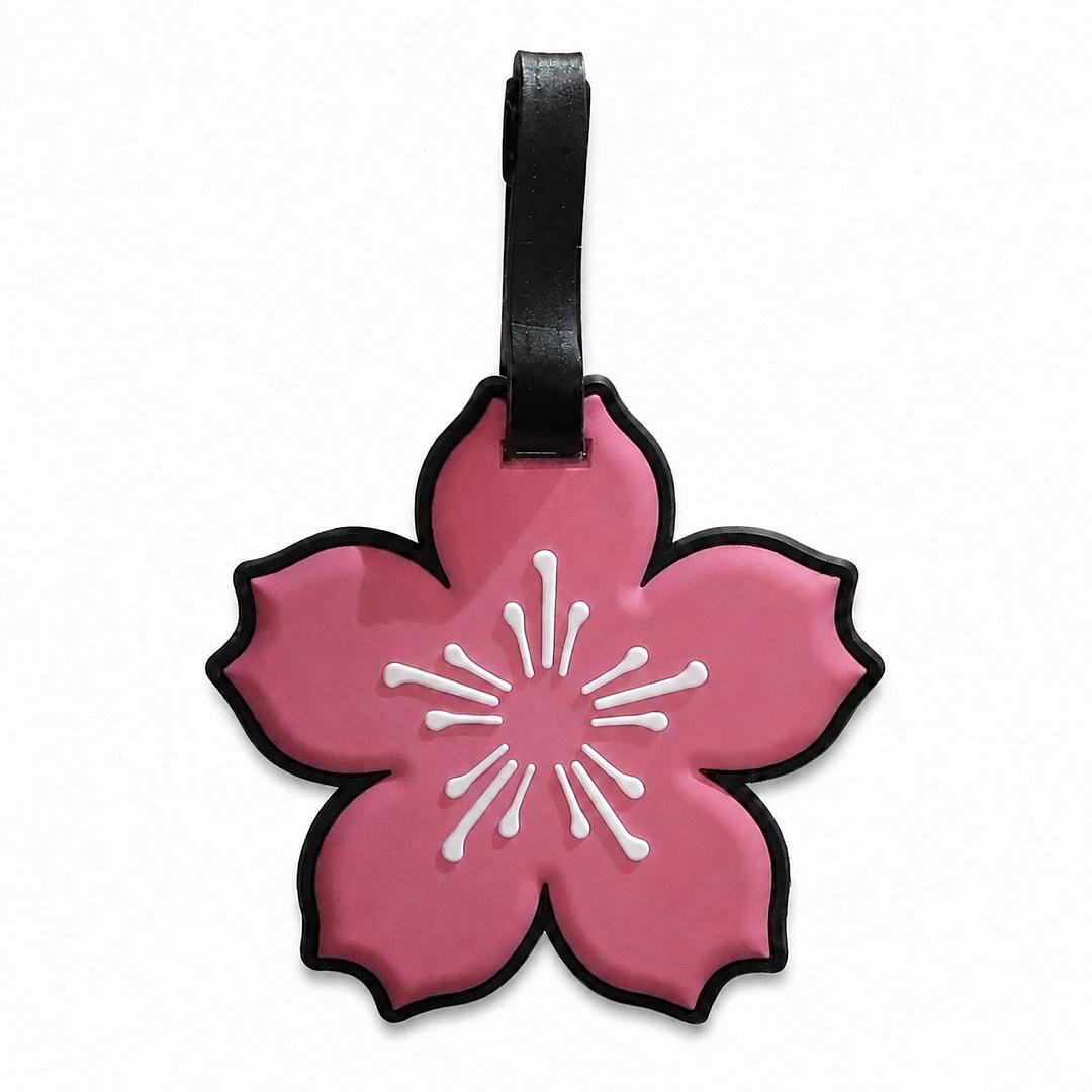 A pink cherry blossom-shaped luggage tag with a black strap, featuring a white stylized flower center and black border on a white background.
