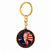 A gold-colored metal keychain featuring a round medallion with Donald J. Trump's portrait, a U.