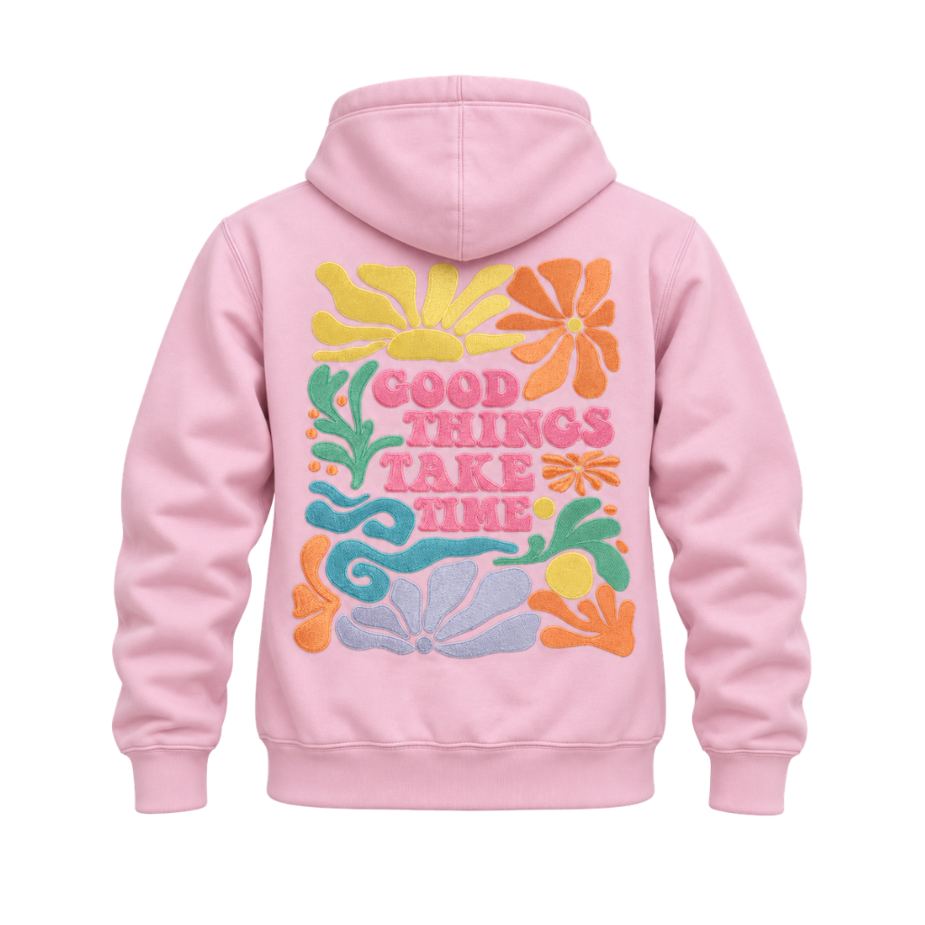 A light pink pullover hoodie shown from the back, featuring a colorful retro-style graphic with flowers and the text 'GOOD THINGS TAKE TIME' in pink, yellow, orange, green, and blue.