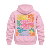 A light pink pullover hoodie shown from the back, featuring a colorful retro-style graphic with flowers and the text 'GOOD THINGS TAKE TIME' in pink, yellow, orange, green, and blue.
