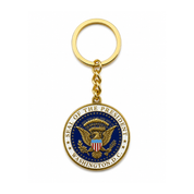 A gold-colored keychain featuring the Seal of the President of the United States in the center, suspended from a gold split ring on a clean white background.