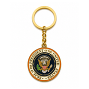 A gold-colored metal keychain featuring the Seal of the President of the United States. The keychain has a gold split ring and chain, with a round medallion charm displaying the official US Presidential seal on a white background.