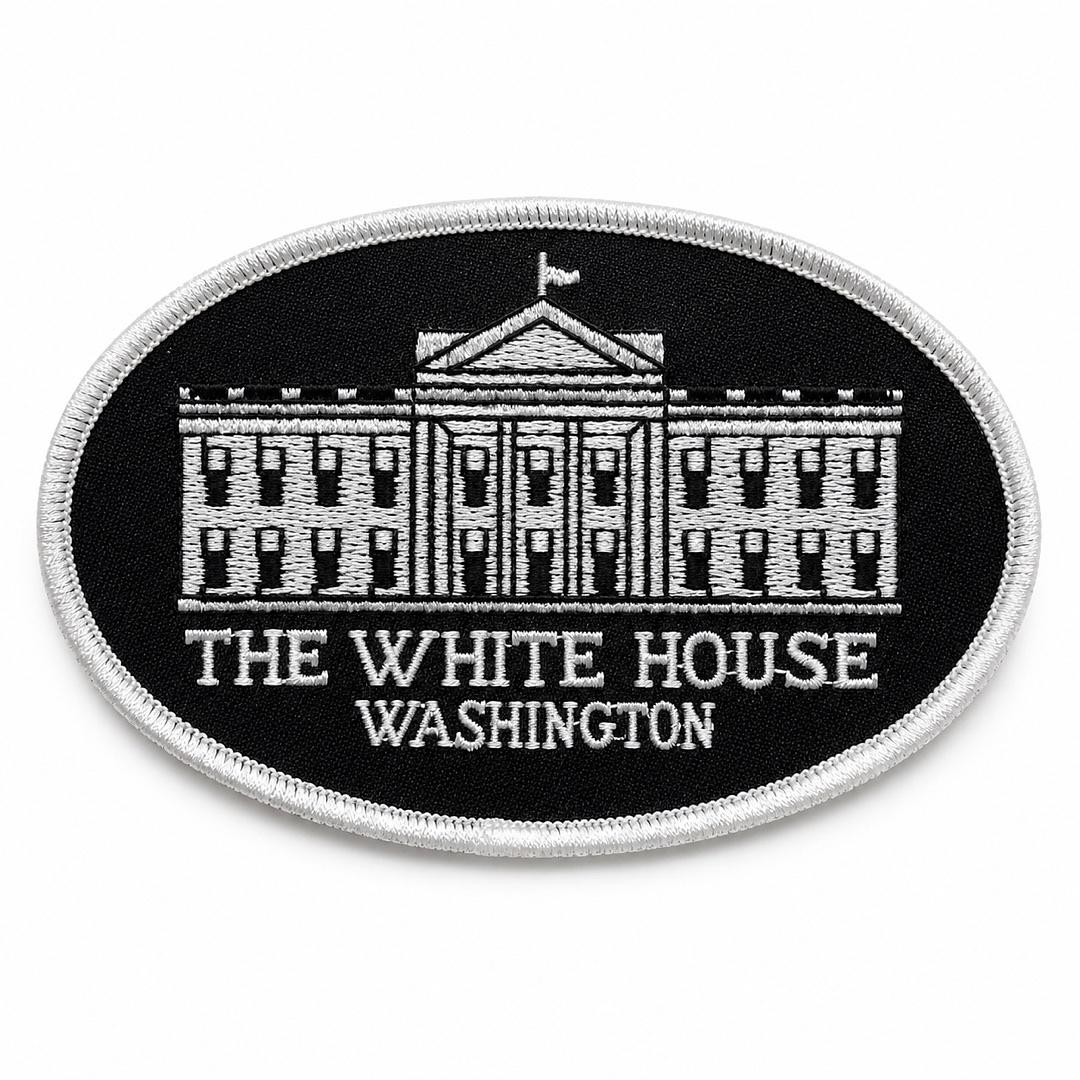 An oval embroidered patch featuring a white line drawing of the White House on a black background, with the text 'THE WHITE HOUSE WASHINGTON' in white below the building. The patch has a white stitched border and is shown on a plain white background.