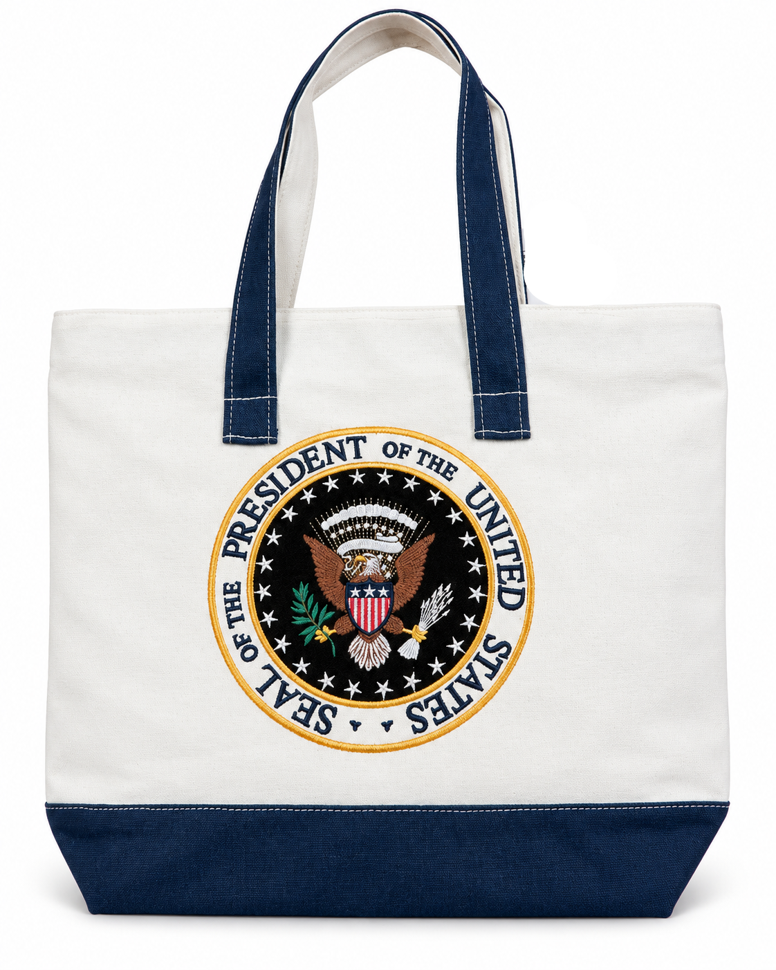 A canvas tote bag with a white body, navy blue handles and bottom trim, featuring a large circular Seal of the President of the United States printed on the front.