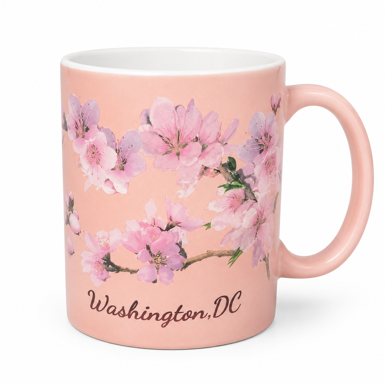 A light pink ceramic mug featuring a watercolor-style print of pink cherry blossoms and the text 'Washington, DC' in brown script near the bottom. The mug has a white interior and a matching pink handle, shown against a plain white background.